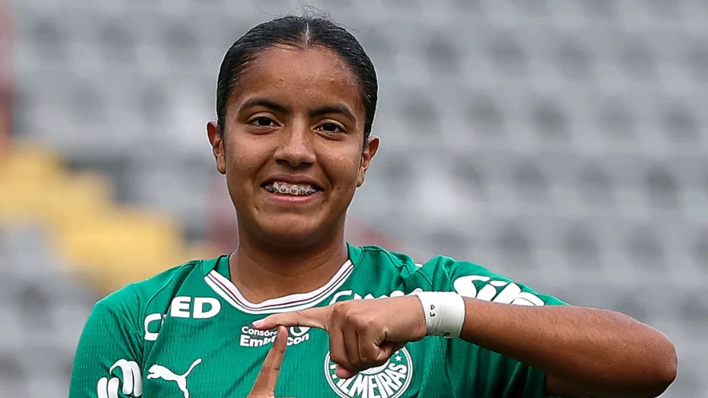 Jogadora do Palmeiras Sub-20 sorri e aponta para o escudo da camisa